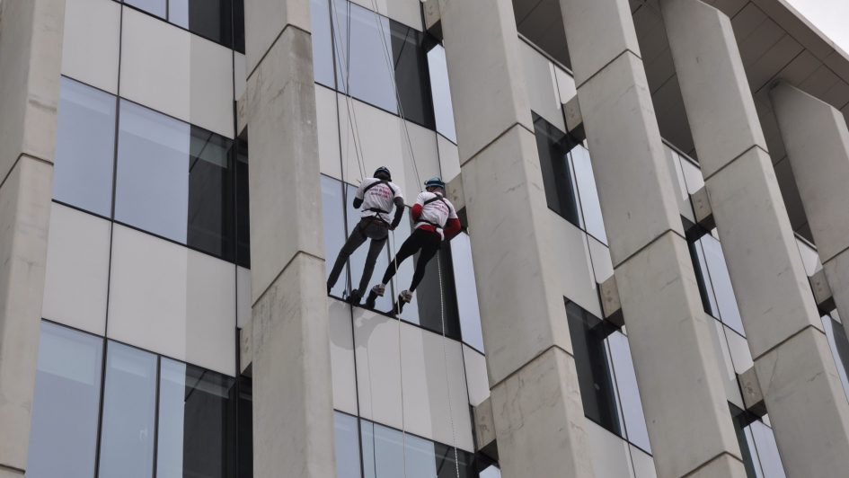 Two people abseiling down a glass and concrete building