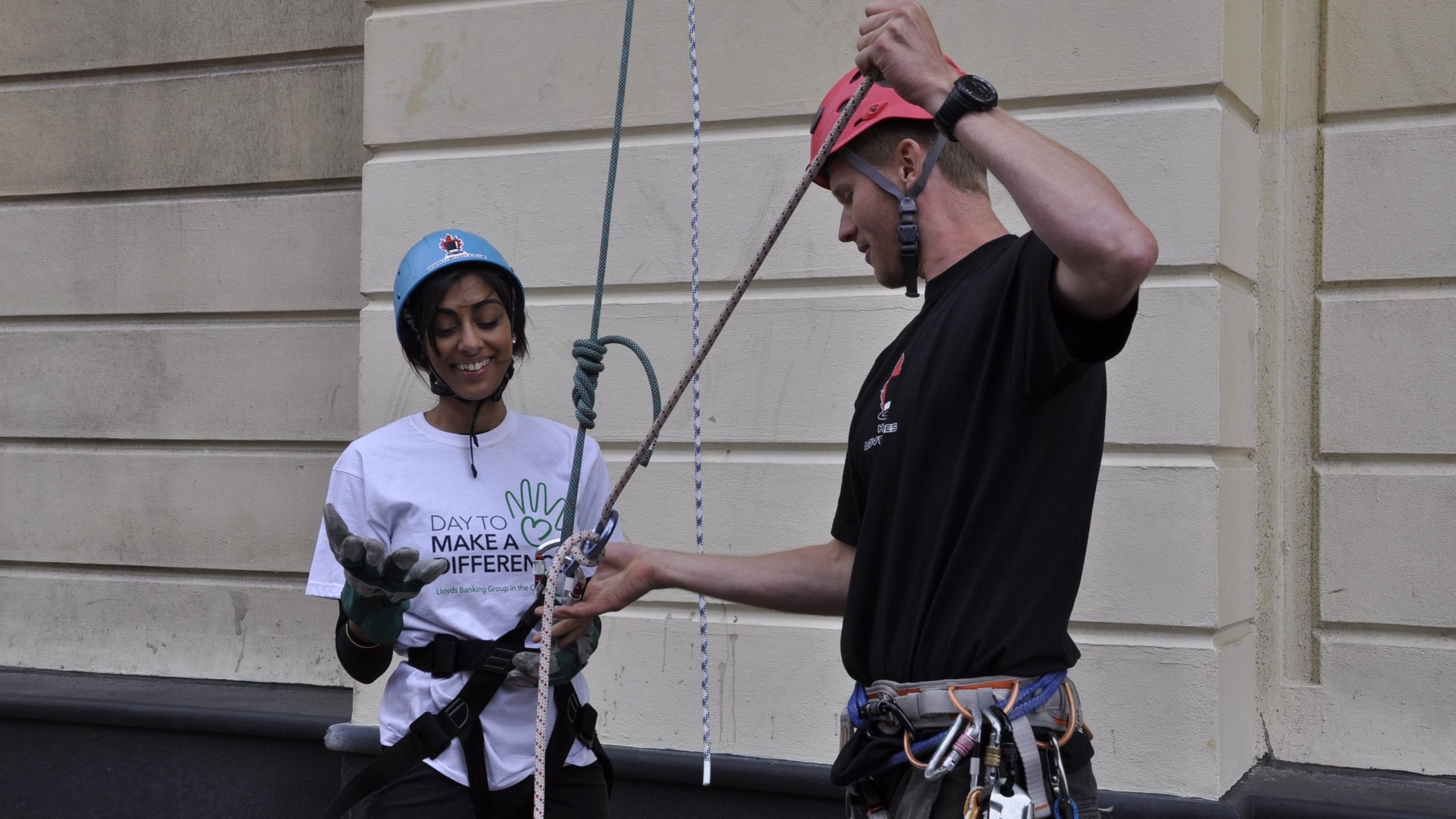 A woman wearing a harness being untied by Tom from her abseil rope.