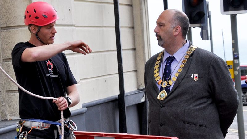 The Mayor of Brighton speaking with Tom, who is gesturing and holding a rope.