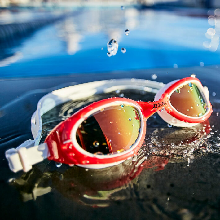Red zone 3 swimming goggles with a white strap and reflective lens. Action shot.