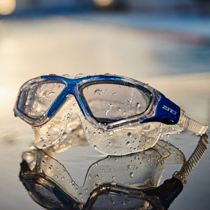 Clear swimming goggles with blue accents around the nose section. Rendered image.