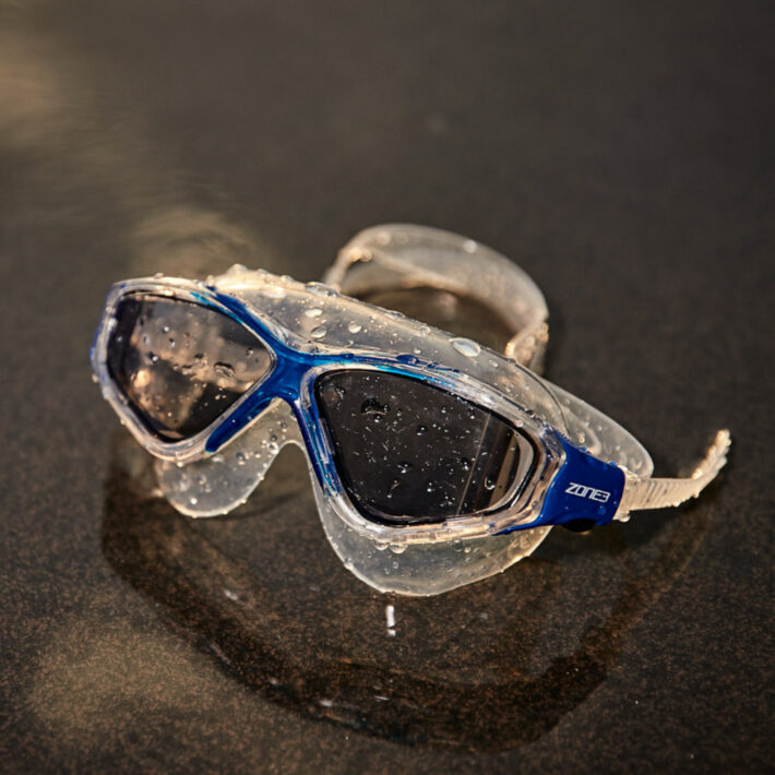 Clear swimming goggles with blue accents around the nose section. Goggles with water droplets on them.